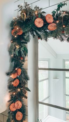 a christmas wreath with oranges and greenery hanging on the wall next to a window