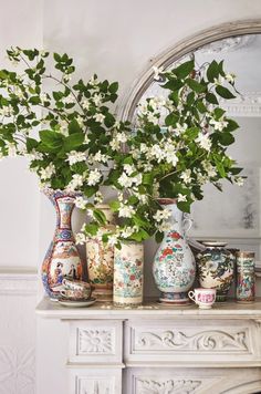 there are many vases with flowers in them on the mantle next to a mirror