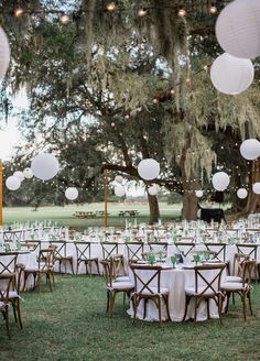 tables and chairs are set up for an outdoor wedding reception with paper lanterns hanging from the trees