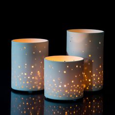 three lit candles sitting next to each other on top of a black surface with gold dots