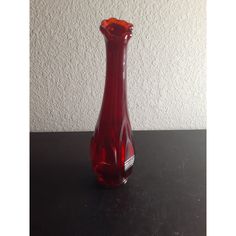 a red glass vase sitting on top of a black table next to a white wall