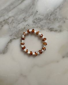 a bracelet with white and brown beads on a marble countertop next to a black bead