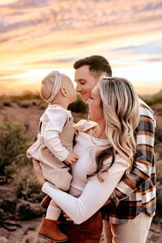 a man and woman holding a baby in their arms while the sun sets behind them