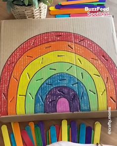 a cardboard box filled with lots of different colored pencils next to a rainbow painting