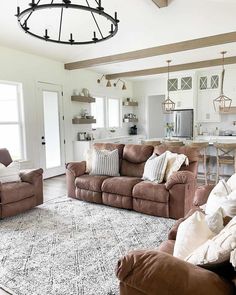 Capped ceiling beams in this farmhouse living room add a rustic look to the bright space. Add a black wagon wheel chandelier for an industrial modernized twist. The rust-brown suede recliner sofas give this space an ultra-cozy feel...   Image: styled_by_jadeleah