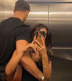 a man and woman standing in front of an elevator taking pictures with their cell phones