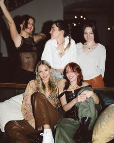 four women are sitting on a couch posing for a photo with their arms in the air