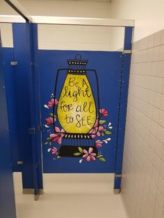 a blue and white bathroom stall with a painting on the wall that says bright for all to see