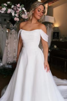 a woman in a white wedding dress looking down at her hand on her hip while standing next to some dresses