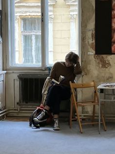 a man sitting at a table in front of a window reading a book while holding his head to his hand