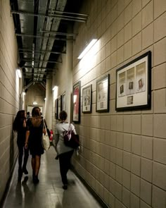 several people walking down a long hallway with pictures on the wall and framed photographs on the walls