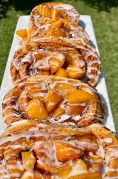 some food is laying out on a long white table outside in the grass and ready to be eaten