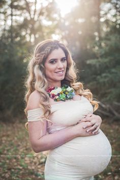 a pregnant woman with flowers in her hair is posing for a photo while holding her belly