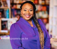 a woman with braids is smiling at the camera in front of bookshelves