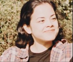 a young woman is smiling in front of some bushes and trees with her eyes closed