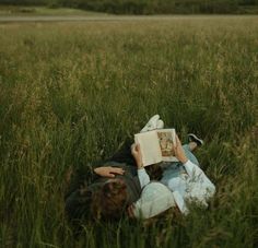 two people laying in the grass reading a book