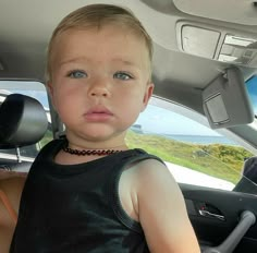 a little boy sitting in the back seat of a car looking at the camera man