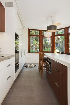 a kitchen with wooden cabinets and white counter tops next to a dining room table in front of two large windows