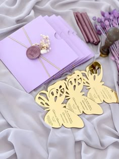 purple and gold wedding stationery on a white bed with lavender flowers in the background