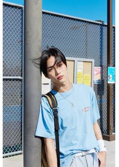 a young man leaning against a pole wearing a blue t - shirt and suspenders