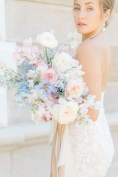 a woman in a wedding dress holding a bouquet of flowers with her back to the camera