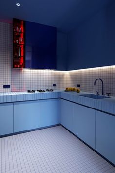 an empty kitchen with blue cabinets and white tiles on the walls, along with red lights