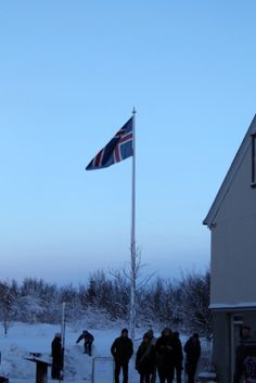 several people are standing in the snow near a flag pole and some buildings with flags on it