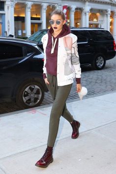 a woman walking down the sidewalk in front of a building wearing sunglasses and a hoodie