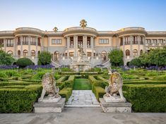 a large building with hedges in front of it and statues on the ground near by