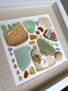 sea glass and seashells are displayed in a shadow box on the table top