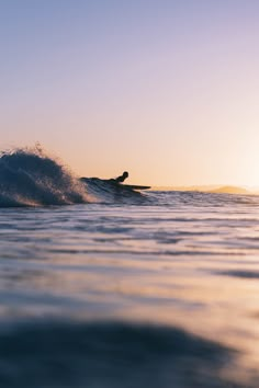 a person riding a surfboard on top of a wave in the ocean at sunset