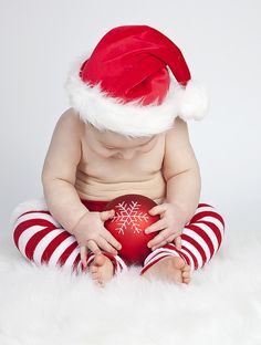 a baby wearing a santa hat and holding a red ball