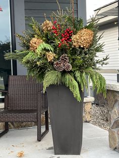 a large potted plant with pine cones, berries and greenery on the front porch