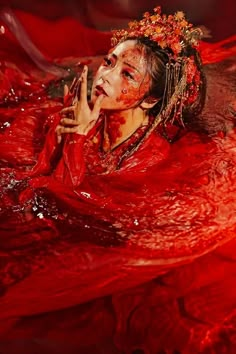 a woman with red paint on her face and hands in the water, wearing a headdress