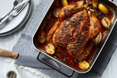 a roasting pan filled with chicken, potatoes and onions next to a knife and fork