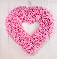 a heart shaped pink rosette wall hanging on a white wooden wall with the word love spelled in it