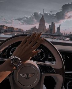 a woman's hands on the steering wheel of a car in front of a city skyline