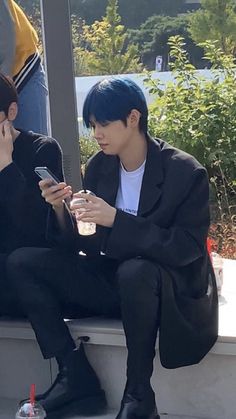 two young men sitting next to each other while looking at their cell phones