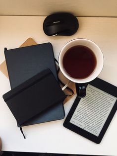 there is a cup of tea next to an electronic device and a book on the table