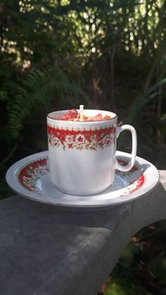 a cup with a candle in it sitting on a saucer next to some trees