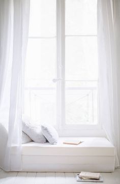 a white window seat sitting in front of a window with curtains on the windowsill