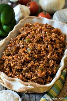 a dish filled with rice and vegetables on top of a wooden table next to green peppers