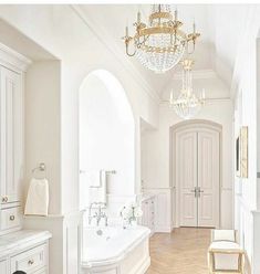 a white bathroom with chandelier and bathtub in the middle of the room