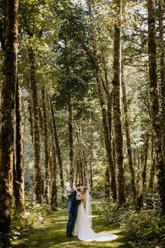 a bride and groom standing in the middle of a forest with their arms around each other