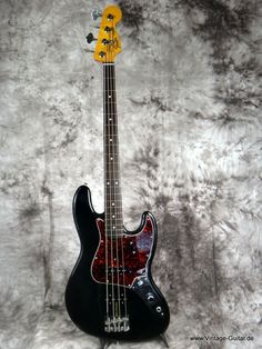 a black and yellow bass guitar sitting on top of a white background with red spots