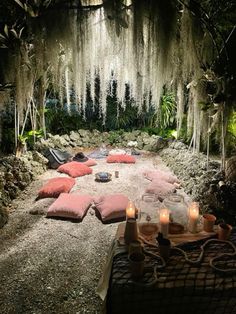 an outdoor seating area with candles and pillows on the ground in front of moss covered trees