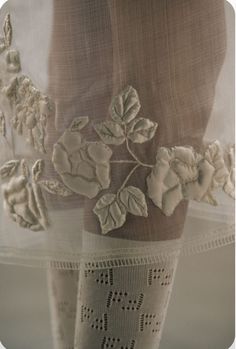 an embroidered piece of cloth with flowers and leaves attached to the side of a sheer curtain