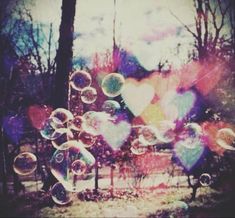 soap bubbles are floating in the air near trees and hearts shaped shapes on a sunny day