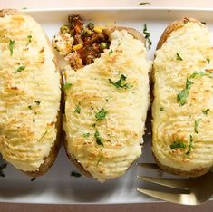 three loaded baked potatoes on a white plate with a fork and knife next to it