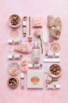 an assortment of cosmetics and seashells laid out on a pink surface with shells